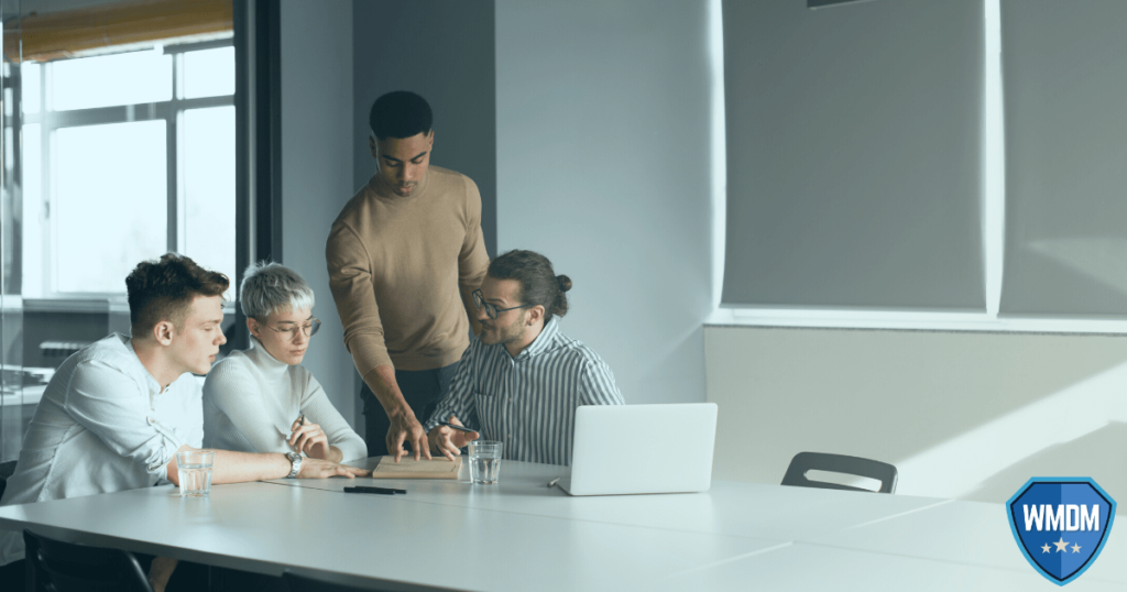 Man presenting to three seated individuals in a boardroom.