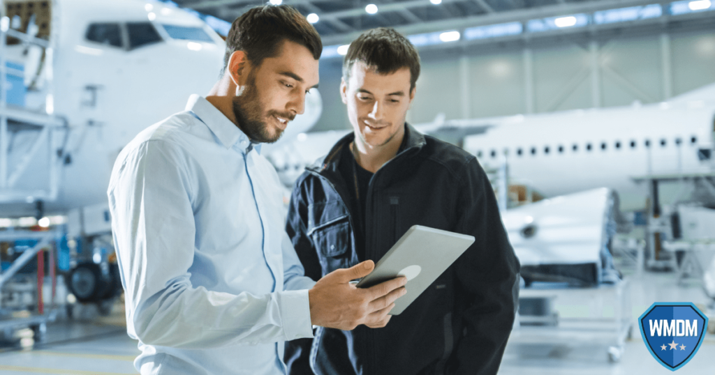 Wingmanning to have your back. Two men standing in aircraft hangar looking at a tablet.